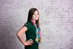 Redhead preteen girl wearing Disney race shirt and Disney race medals smiling in front of a brick wall in Winter Garden Florida
